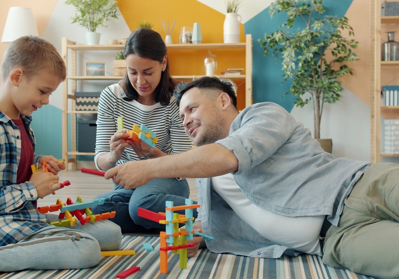 Family building with colorful toy blocks together on floor.
