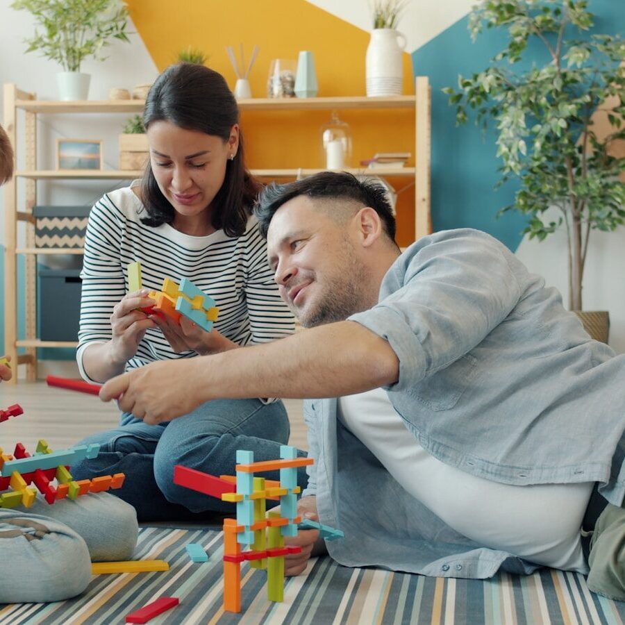Family building with colorful toy blocks together on floor.