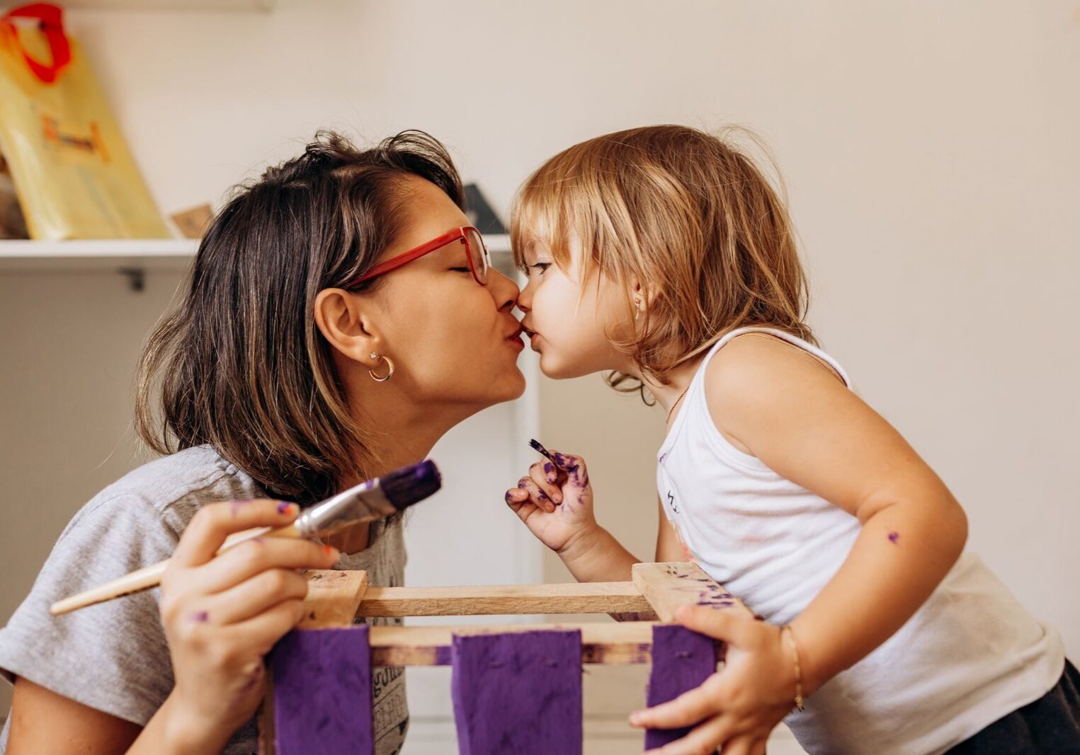 A joyful mother and daughter share a playful moment while painting art projects indoors.