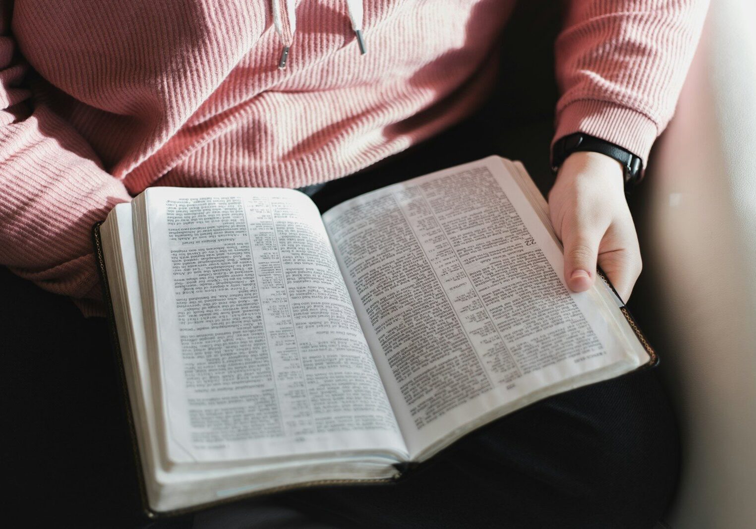 person in pink and white striped long sleeve shirt reading book